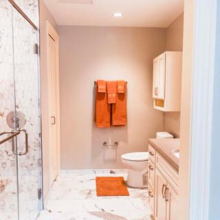 A modern bathroom with orange towels, featuring a shower, sink, and marble flooring.