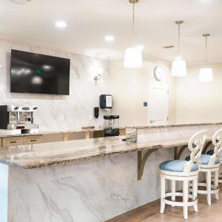 A modern kitchen area featuring a marble countertop with bar stools, a wall-mounted television, and a coffee machine.