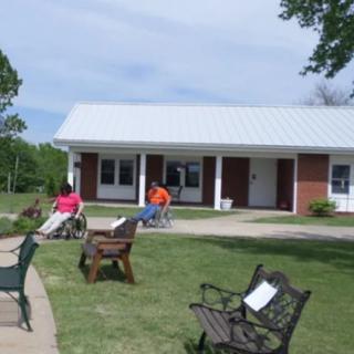 People relaxing on benches in a park area with a small building in the background.