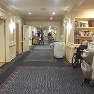 A well-lit hallway featuring bookshelves, a wheelchair, and cleaning equipment.