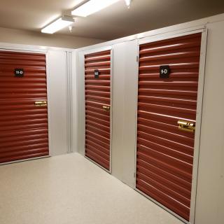 A well-lit corridor with multiple storage units featuring red shuttered doors.