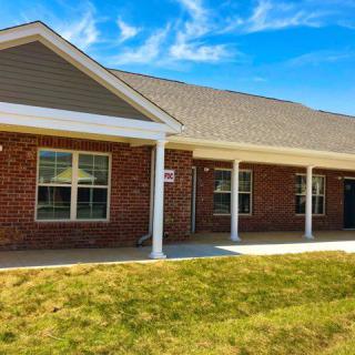 A brick residential house with a porch and lawn on a sunny day.