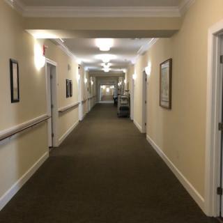 A long indoor hallway with carpeted flooring and multiple doors, featuring soft lighting and framed pictures on the walls.