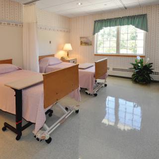 A clean and well-lit hospital patient room with two beds, equipped with lamps and a window providing natural light.