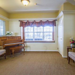 A cozy living room with a piano and seating area near a window.