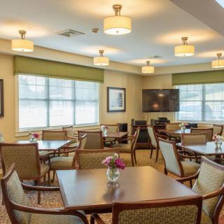 A well-lit dining area with multiple tables and chairs, featuring large windows and ceiling lights.