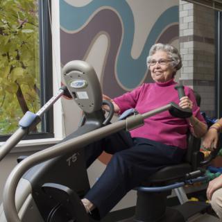 An elderly woman enjoying a workout on a recumbent bike indoors.