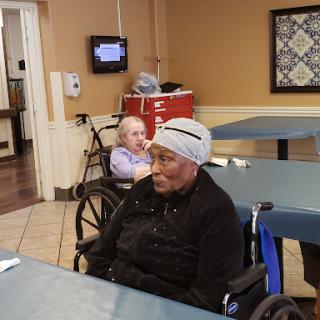 Two elderly individuals in a care facility, sitting in wheelchairs.