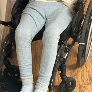 A person sitting in a wheelchair indoors with gray leggings and socks.