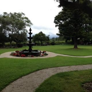 A tranquil garden scene featuring a central fountain surrounded by lush greenery and pathways.