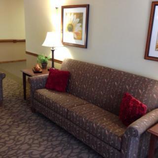 A cozy living room area featuring a patterned sofa with red cushions, a side table with a lamp, and framed artwork on the wall.