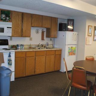 A small kitchen and dining area with wooden cabinets, a refrigerator, microwave, sink, and a round dining table with chairs.