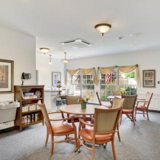 A cozy dining area featuring wooden tables and chairs, illuminated by natural light and decorative fixtures.