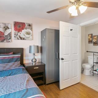 A cozy bedroom featuring a striped bedspread, modern furniture, and an adjacent bathroom.