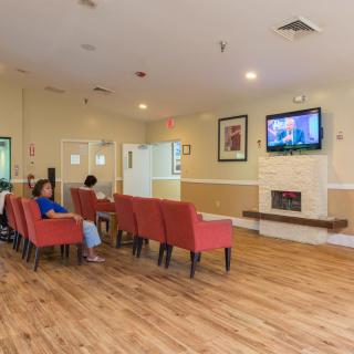 A lounge area with people seated in red chairs watching television.