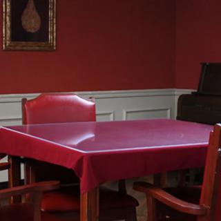 A dining room with red walls, featuring a square table covered with a red tablecloth and surrounded by wooden chairs. A painting hangs on the wall.