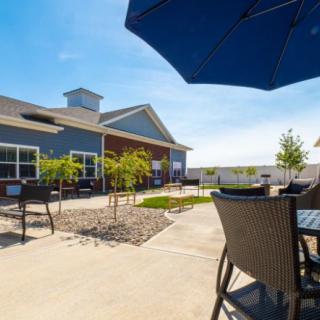 A sunny patio with outdoor furniture and an umbrella, adjacent to a modern building.