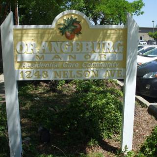 A sign for the Orangeburg Library against a backdrop of a parking lot and trees.