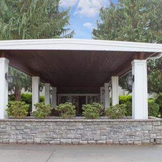 A covered building entrance with white columns and surrounding greenery.