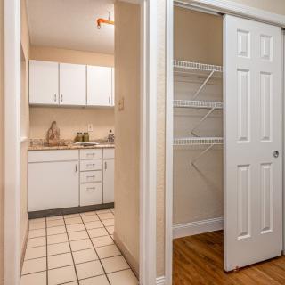 A view of a kitchen with white cabinets and a nearby closet with shelving.