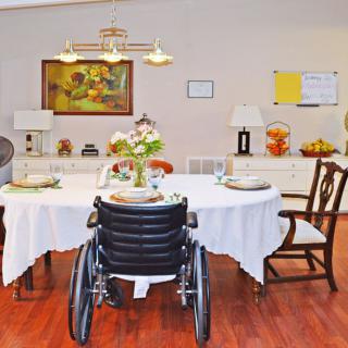 A warm and inviting dining room setup with a wheelchair placed at a table set for dinner, surrounded by elegant decor and artwork.