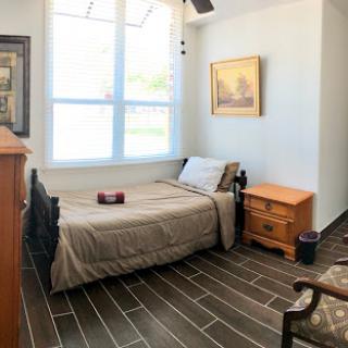 A cozy bedroom featuring a bed with neutral bedding, natural light streaming through the window, and wooden accents.
