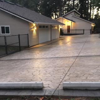 A view of a house with a spacious concrete driveway and garage, illuminated by outdoor lighting in the evening.