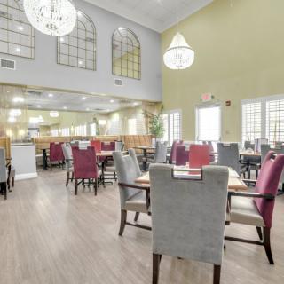 A spacious dining room with elegant chandeliers, featuring multiple tables and chairs in a well-lit, inviting restaurant setting.