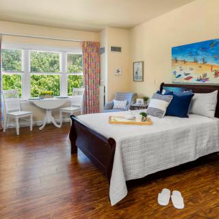 A cozy bedroom with a large bed, wooden flooring, and a bright window view.