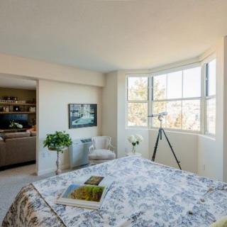 A cozy bedroom featuring a large window with abundant natural light, decorated with floral bedding, a telescope, and indoor plants.