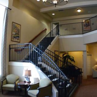 A cozy interior space featuring a staircase with black railings, a small seating area with chairs and a lamp, and decorative plants.