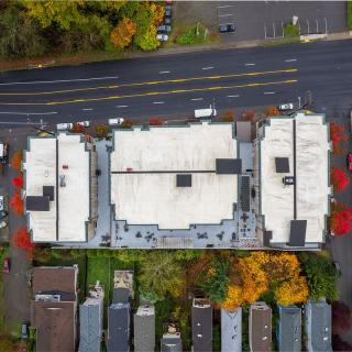 Aerial view of buildings with a road and parking lot, surrounded by autumn trees.