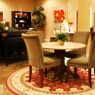 A well-decorated dining room featuring a round table with chairs, surrounded by a patterned rug and complemented by plants and artwork.
