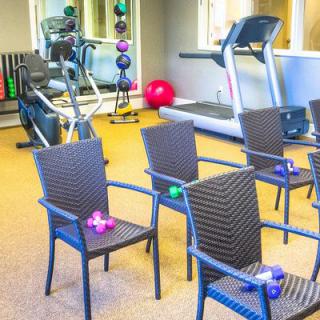 A brightly lit fitness center featuring a treadmill and chairs with colorful dumbbells.