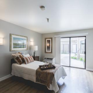 A modern and minimalist bedroom with natural light streaming through a sliding glass door.