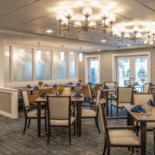 A well-lit dining room with elegant chandeliers and neatly arranged tables and chairs.