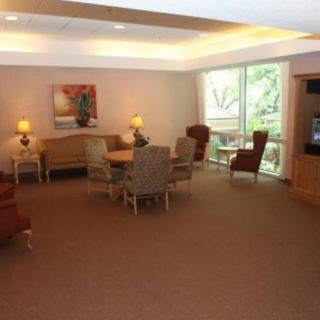 A cozy living room with a seating area featuring a table, several chairs, sofas, and lamps, complemented by a large window and decorative elements.