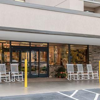 The image shows the entrance of a building with several white rocking chairs outside.