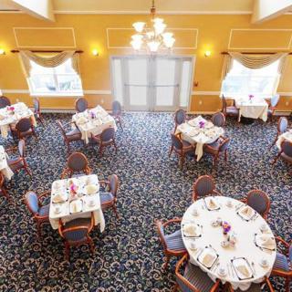 An elegant dining room with multiple tables set for a meal, featuring chandeliers and large windows.