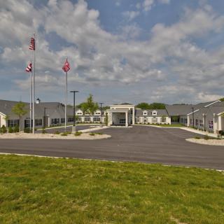 A modern building with flags flies in front and a well-maintained grassy area under a partly cloudy sky.