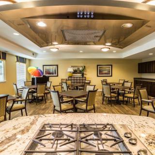 A spacious dining area with multiple tables and chairs, featuring a central kitchen island and ceiling fan.