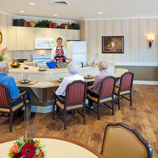 A group of seniors gather around a kitchen counter for a cooking demonstration in a community setting.