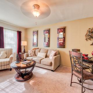 A cozy living room with a beige sofa, armchair, and round coffee table, complemented by wall art and adjacent dining space.
