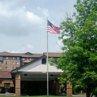 An American flag waves on a flagpole in front of a building and trees.