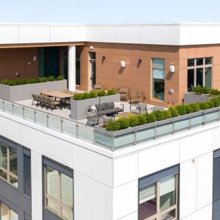 Modern rooftop terrace with seating and greenery on a city building.