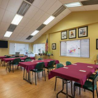A well-lit dining area featuring several tables with maroon tablecloths, set up for a gathering or event.