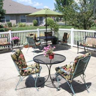 A sunny patio area with outdoor furniture and vibrant cushions, surrounded by a white fence.