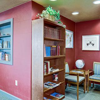 A cozy waiting room with a bookshelf filled with books, artwork on the walls, and seating area with chairs.