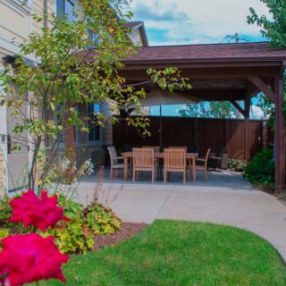 A cozy backyard patio with a pergola and outdoor seating, surrounded by a lush garden and vibrant flowers.