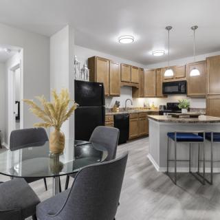 A modern kitchen and dining area featuring wooden cabinets, a glass table, and pendant lighting.